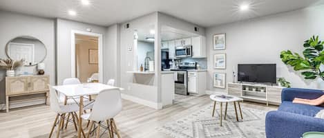 A modern apartment with a dining area, kitchen, living room, and a TV.