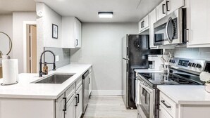 A modern kitchen with white cabinetry, stainless steel appliances, and a central island with a sink. - "The Cozy Cabana" in Paseo (Oklahoma City)