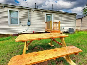 A wooden picnic table set up in front of a house with a window and a door.