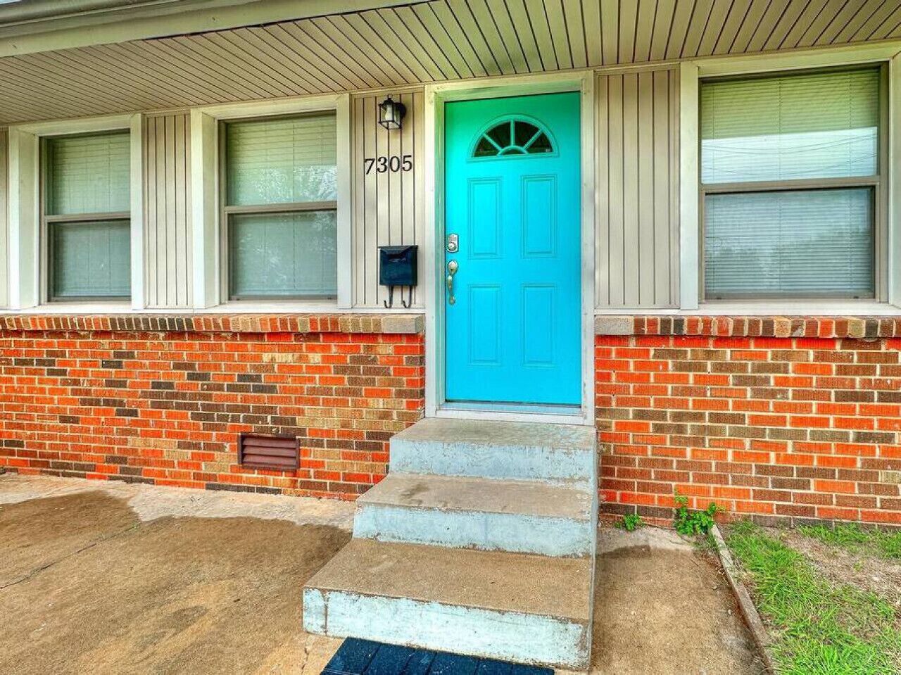 A house with a blue door, numbered 7305, and a brick exterior.