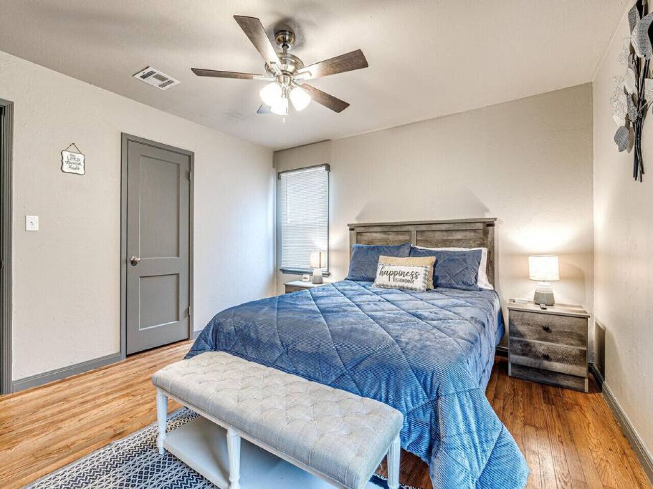 A bedroom with a bed, a bench, a nightstand, a ceiling fan, and a window.
