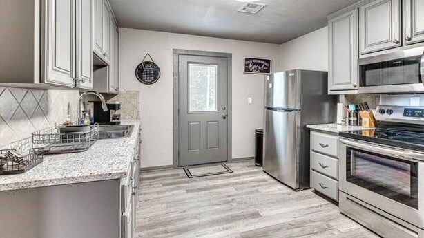 A modern kitchen with stainless steel appliances, a granite countertop, and light wood flooring.