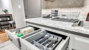 A kitchen with a built-in dishwasher, a countertop with a sink, and a storage drawer with utensils.