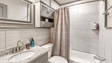 A bathroom with a double sink, toilet, and bathtub. There are toiletries on the counter and a shower curtain.