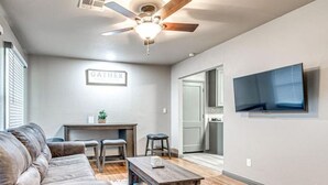 A living room with a sofa, coffee table, and a ceiling fan. There is a sign on the wall that says "GATHER".