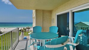 A balcony with a table and chairs, overlooking a beach and ocean. - Regency Towers by Resort Collection (Panama City Beach)