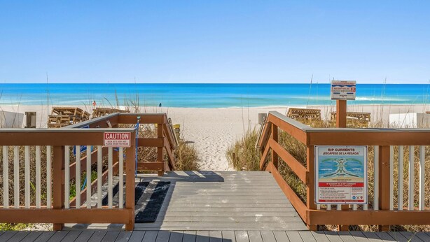 A wooden boardwalk leading to a beach with a caution sign and a rip current warning sign. - Regency Towers by Resort Collection (Panama City Beach)
