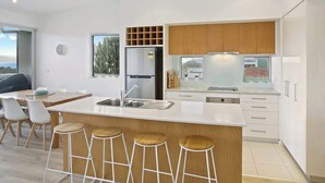 A modern kitchen with a central island, bar stools, a refrigerator, and a large window. - Bay Vue - Absolute Oceanviews! (Apollo Bay)