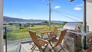 A balcony with a grill, chairs, and a view of a lake and hills. - Bay Vue - Absolute Oceanviews! (Apollo Bay)