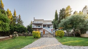 Una casa de dos pisos con un sendero de piedra que lleva a la entrada, rodeada de follaje y árboles.