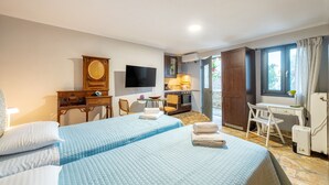 Habitación de hotel con dos camas, un escritorio con silla, televisión, armario y ventana con cortinas.
