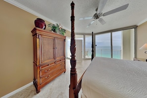 A bedroom with a four-poster bed, a wooden dresser, a ceiling fan, and a view of the ocean. - The Pearl of Navarre #1505 by Southern Vacation Rentals (Navarre)