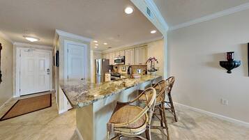 A kitchen with a marble countertop, stainless steel appliances, and wicker bar stools.