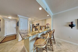 A kitchen with a marble countertop, stainless steel appliances, and wicker bar stools. - The Pearl of Navarre #1505 by Southern Vacation Rentals (Navarre)