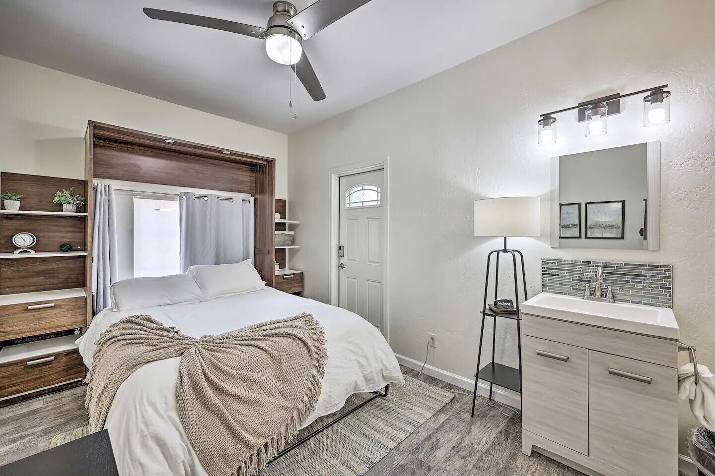 A bedroom with a bed, bedside tables, a wardrobe, a ceiling fan, a bedside lamp, a nightstand, and a window with curtains.