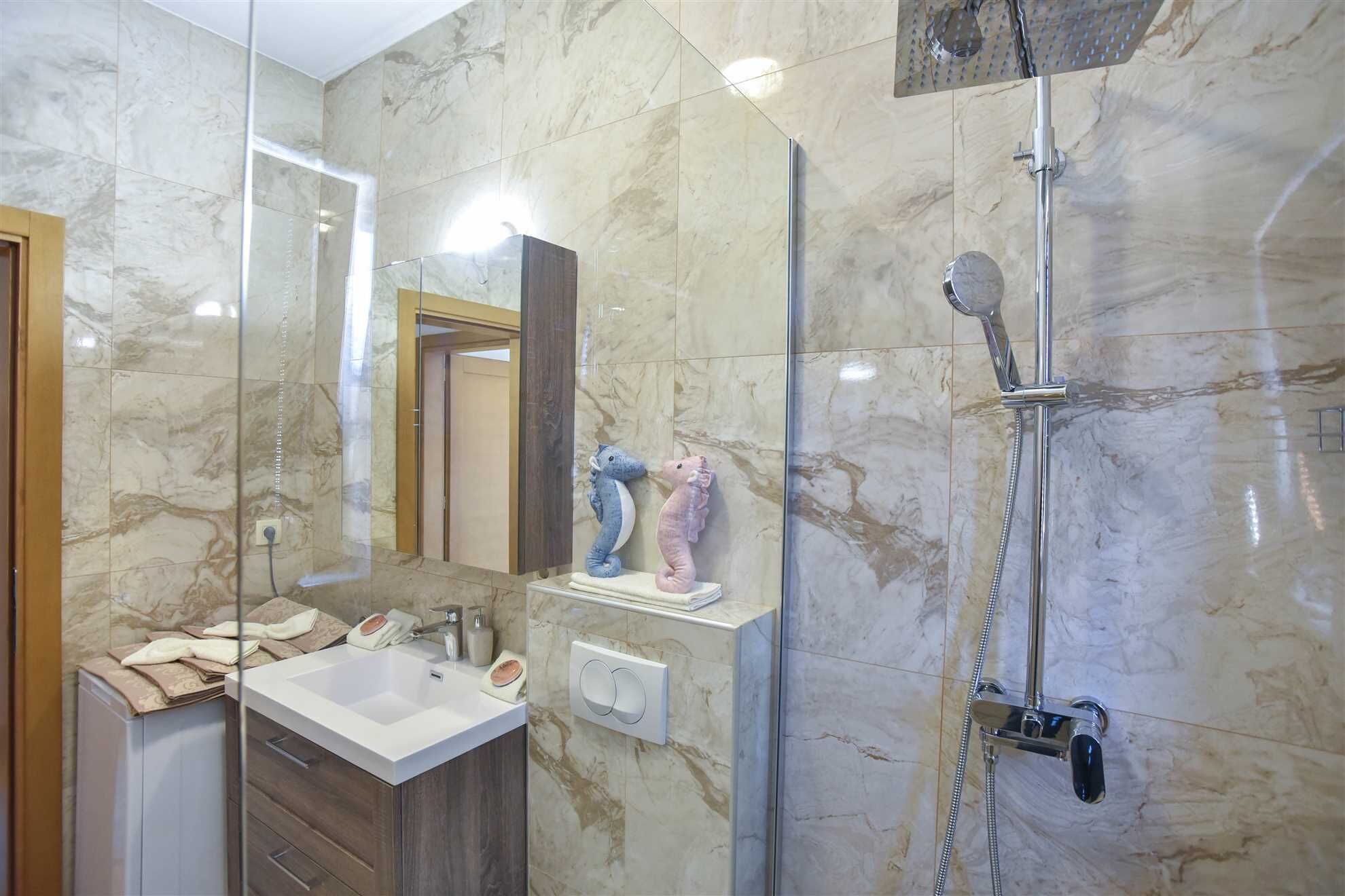 A bathroom with a marble floor, a glass shower enclosure, a white sink, and a mirror.