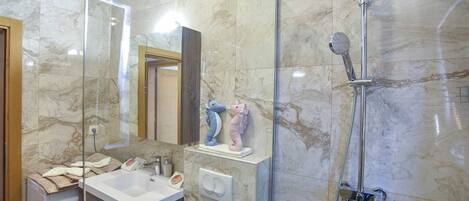 A bathroom with a marble floor, a glass shower enclosure, a white sink, and a mirror.