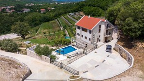 Una casa a due piani con tetto in tegole rosse, una piscina e un muro di pietra che circonda la proprietà.
