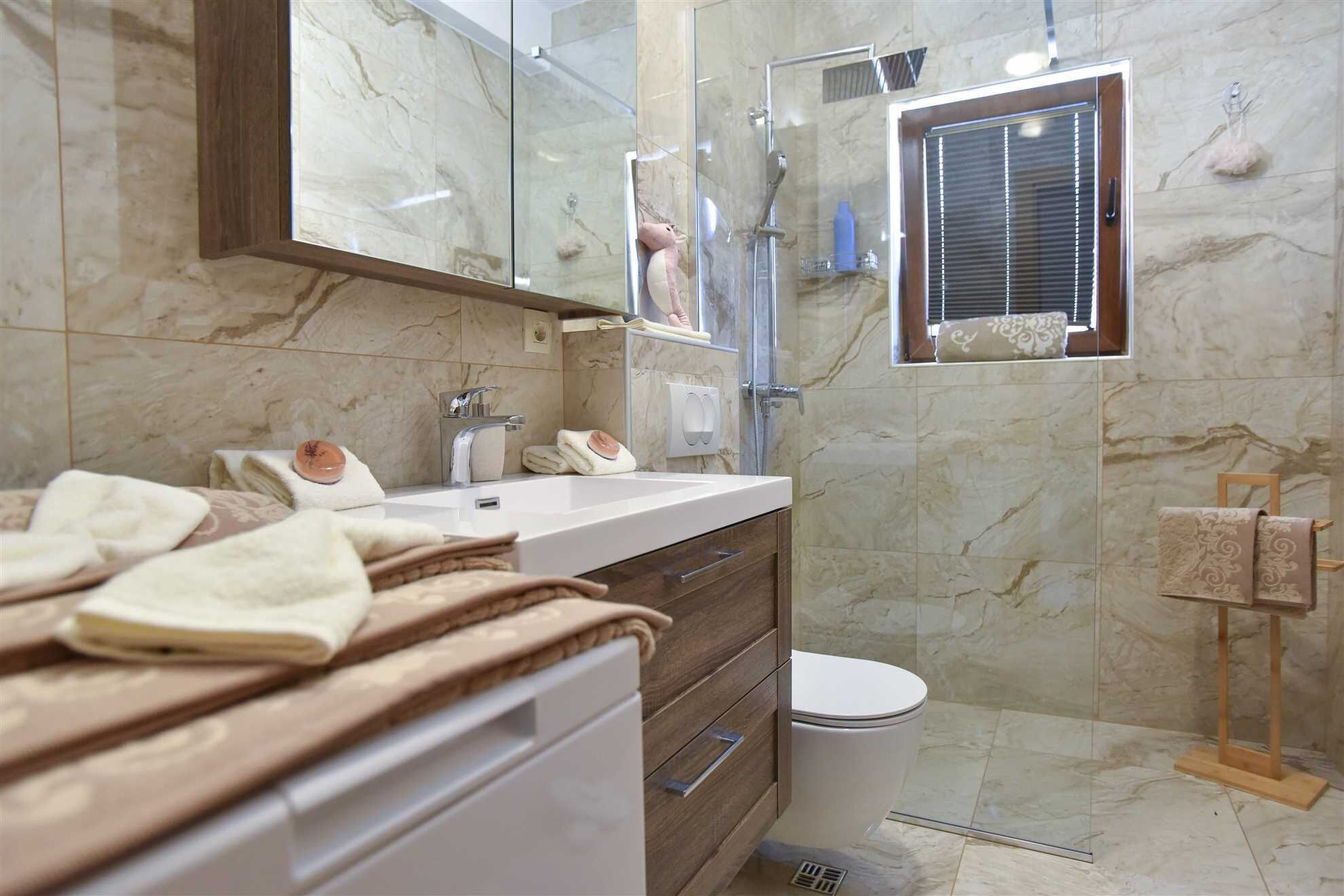 Une salle de bain moderne avec un mur en marbre, un grand miroir, une douche et des toilettes.