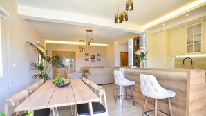 Una cucina moderna con piano di lavoro in legno e sgabelli da bar, una zona pranzo con tavolo e sedie in legno, e un soggiorno con divano e tavolino.