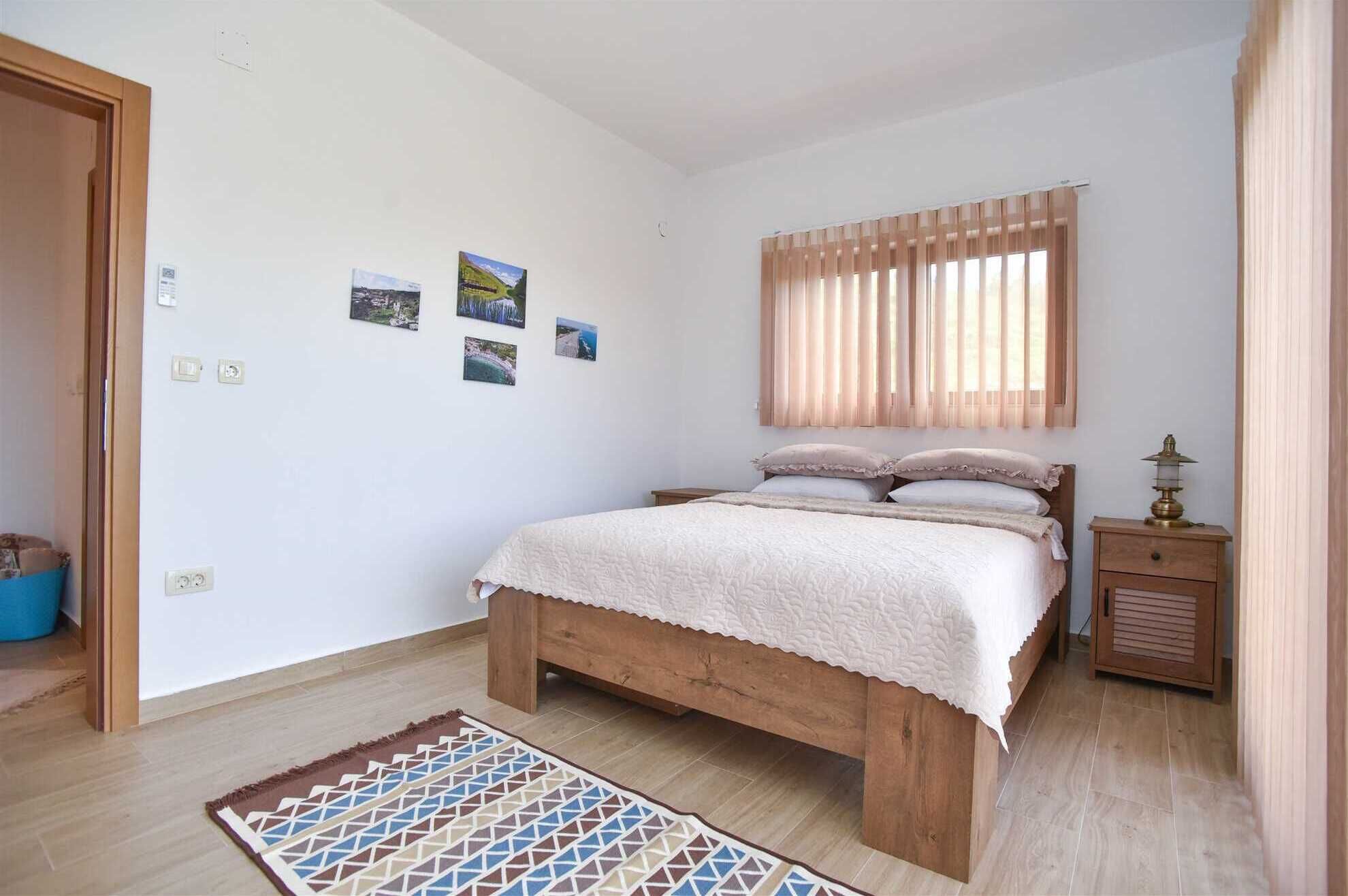 A bedroom with a wooden bed, a nightstand, a lamp, and a window with blinds.