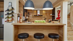 Eine moderne Küche mit Holzschnitzereien, einem Weinregal, einer roten Küchenwaage und drei schwarzen Barhocker.