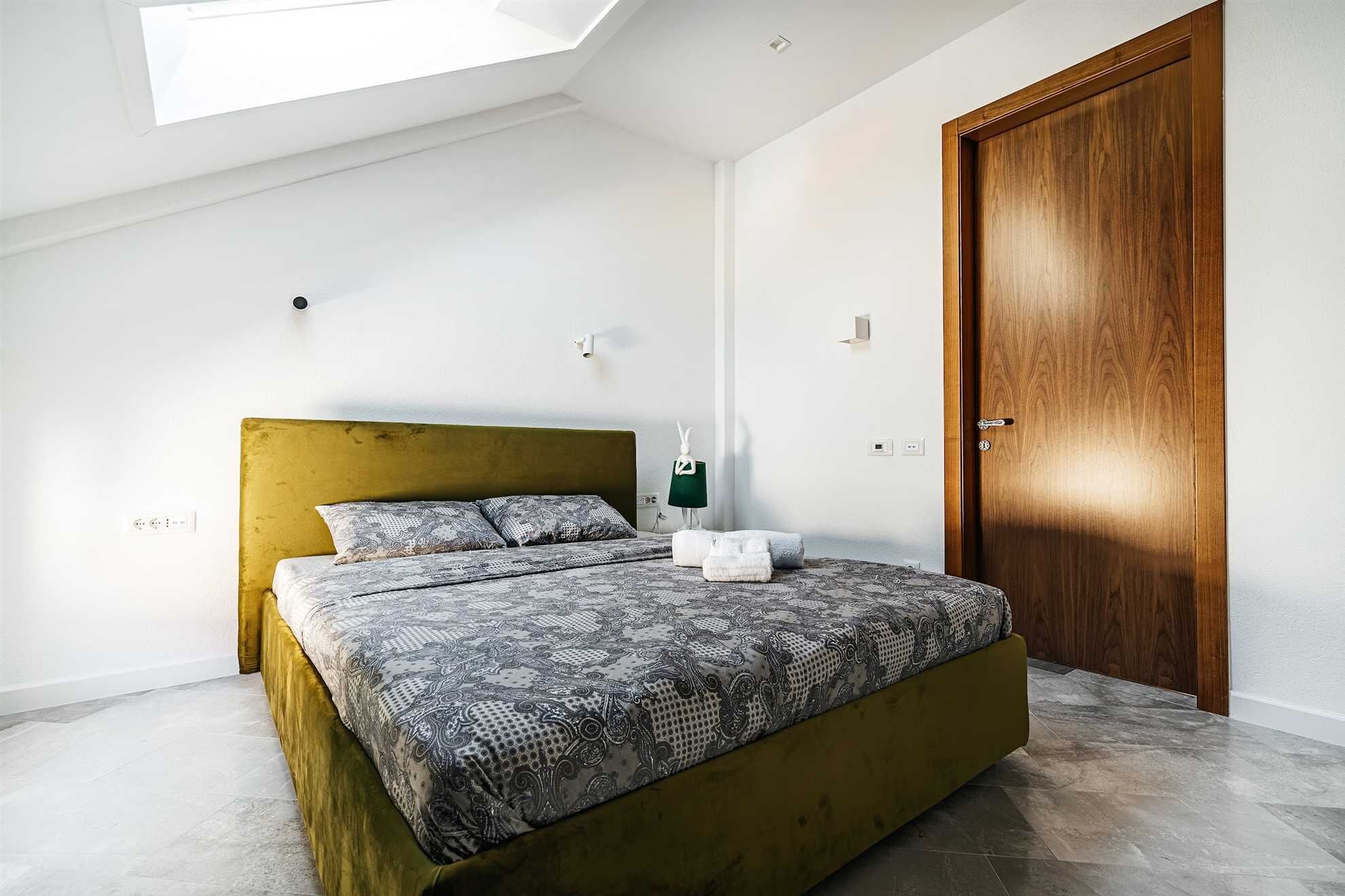 A bedroom with a bed, a wooden door, and a skylight.