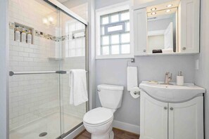 A modern bathroom with a glass shower enclosure, a white toilet, and a vanity with a mirror and sink. - Family Retreat at Village Farmhouse - Near Grand Haven Beach (Spring Lake)