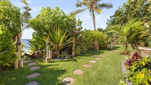 A tropical garden with a stone pathway leading to a wooden deck.