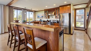 A spacious kitchen with a central island, wooden cabinets, and a large window offering a view of the outdoors.