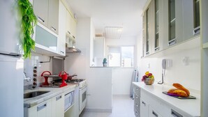 A narrow kitchen with white cabinets, a stove, and a sink. There is a window with a view of the outside. - 3 Bedrooms - Modern - Close to the Mall (São Paulo)