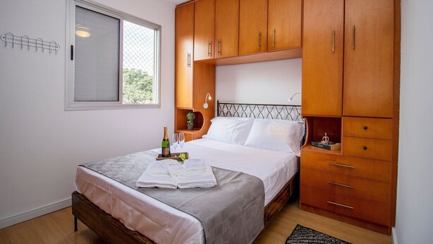 A bedroom with a bed, wooden wardrobe, and a small table with a bottle and glasses. - 3 Bedrooms - Modern - Close to the Mall (São Paulo)