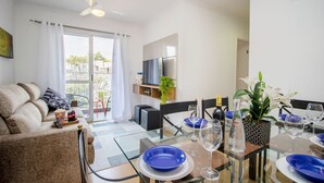A modern living room with a sofa, a dining table set for two, and a TV mounted on the wall. - 3 Bedrooms - Modern - Close to the Mall (São Paulo)