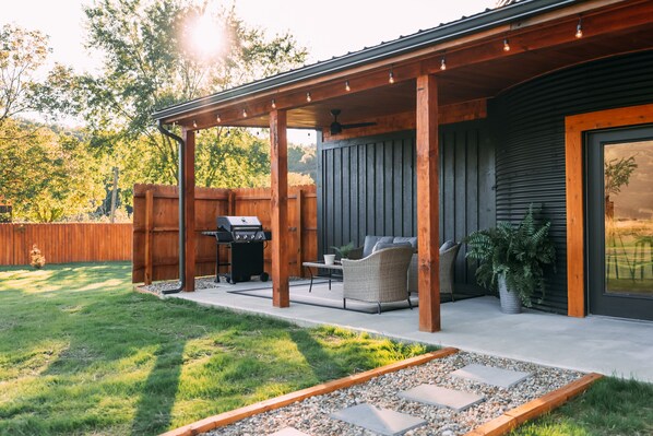 An outdoor patio area with a grill, seating, and a pergola.