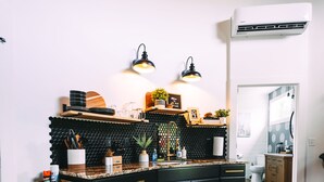 Una cocina con encimera negra, armarios de madera y salpicadero negro. Se observan dos luces empotradas en la pared y un equipo de aire acondicionado blanco.
