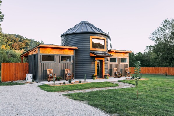 A modern house with a unique cylindrical tower, a wooden deck, and a fenced backyard.