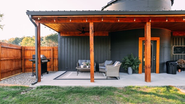 A covered patio area with outdoor furniture, a grill, and a large cylindrical water tank in the background.