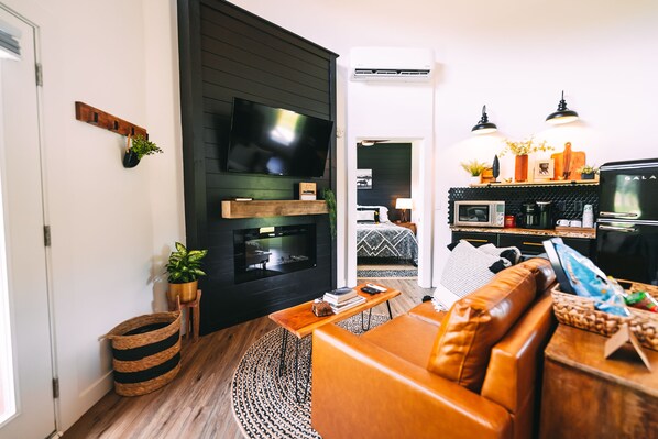 A modern living room with a fireplace, a television, and a kitchen area with a microwave and coffee machine.