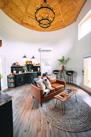 A modern interior with a wooden ceiling, a leather sofa, a dining area, and a kitchen with black cabinets.