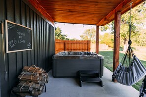 A covered outdoor area with a hot tub, firewood, and a hammock.