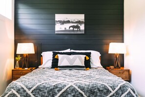 A bedroom with a dark wooden headboard, a bed with a patterned blanket, two bedside lamps, and a framed picture above the bed.