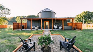 Un patio cubierto con mobiliario exterior y un gran silo de grano al fondo.