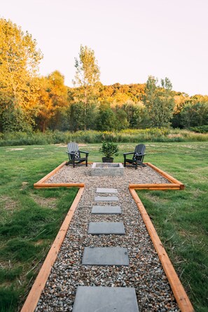 Un sendero de jardín que conduce a dos sillas Adirondack con un brasero en el centro.