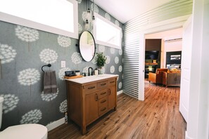 A bathroom with a wooden vanity, a mirror, and a dandelion-patterned wall.