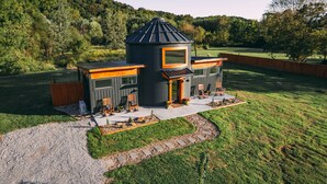 A modern house with a unique conical roof, a patio with outdoor seating, and a well-maintained lawn.
