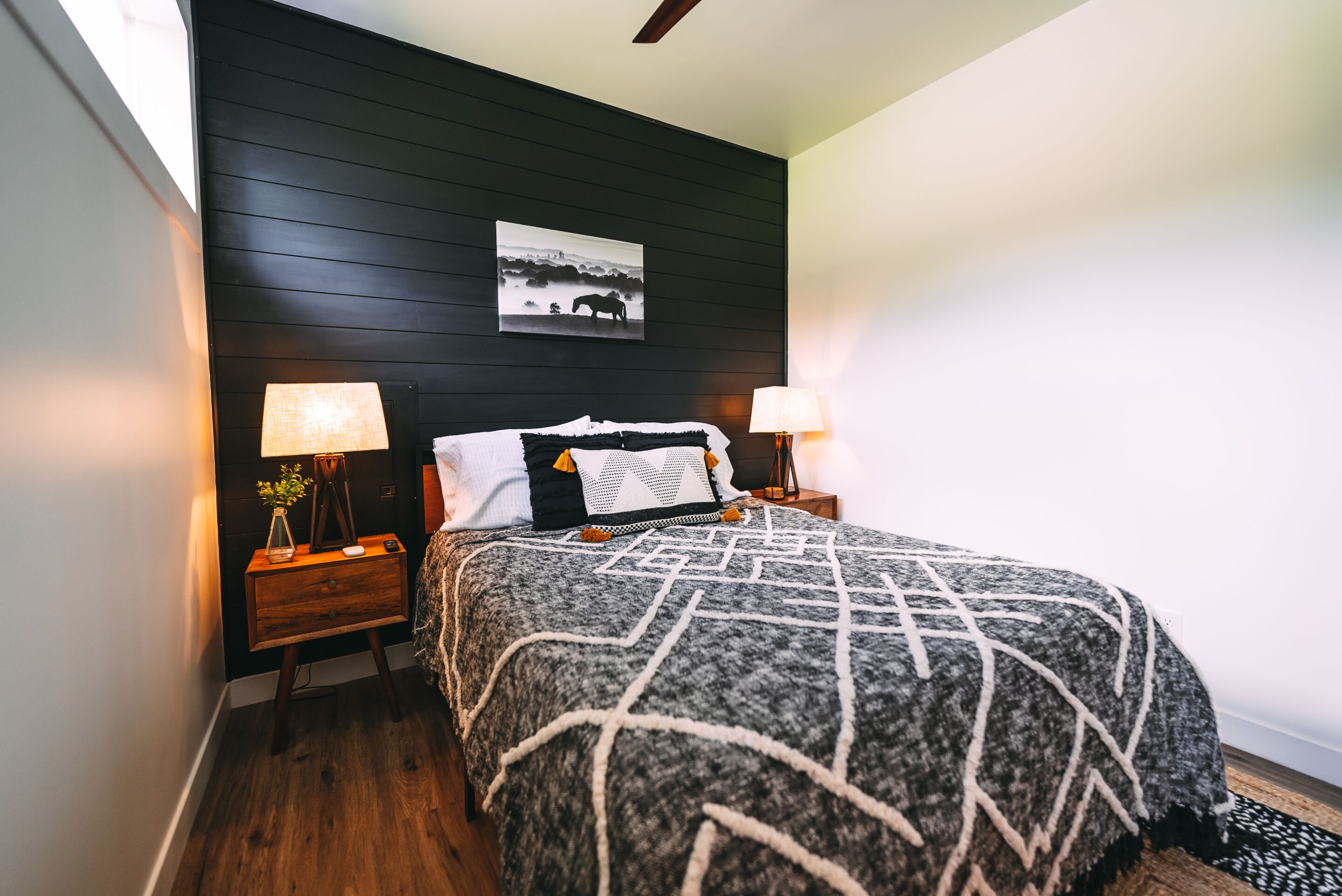 A bedroom with a bed, two bedside tables, a nightstand, a wall-mounted picture, and a lamp.
