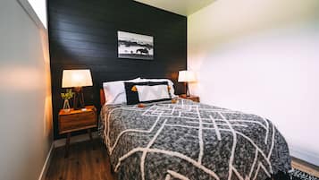 A bedroom with a bed, two bedside tables, a nightstand, a wall-mounted picture, and a lamp.