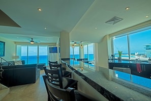 Cozinha moderna com uma ilha grande, área de refeições com cadeiras e vista para o mar.