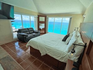 A bedroom with a large bed, a black leather sofa, and a view of the ocean.