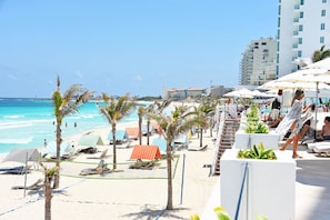 Hotel a la vora de la platja, amb gandules, ombrel·les i zona de piscina.
